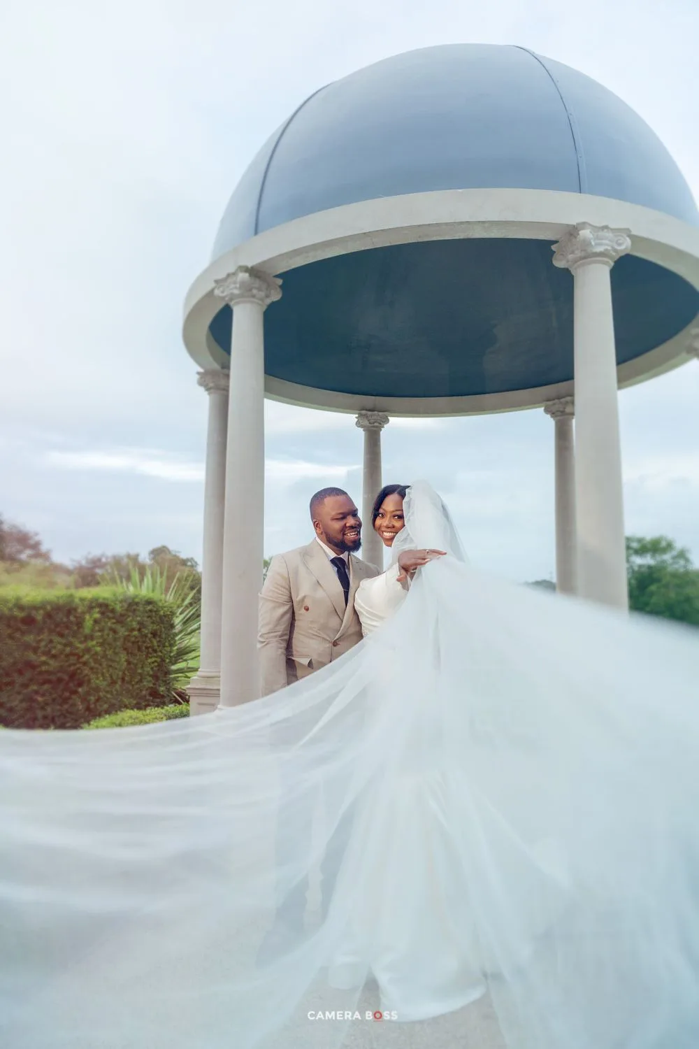 A wedding couple shares a joyful moment under an elegant blue-domed gazebo as the bride's veil flows in the breeze.