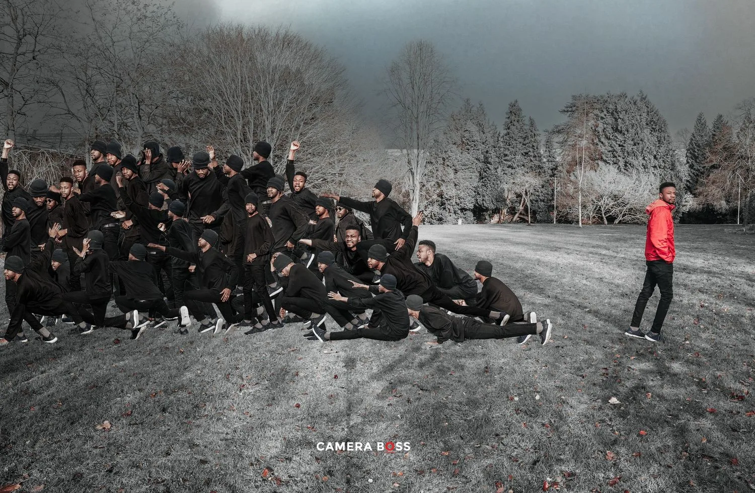 A photographer in red jacket stands out against a monochromatic crowd seated on a snowy hill during a photoshoot.
