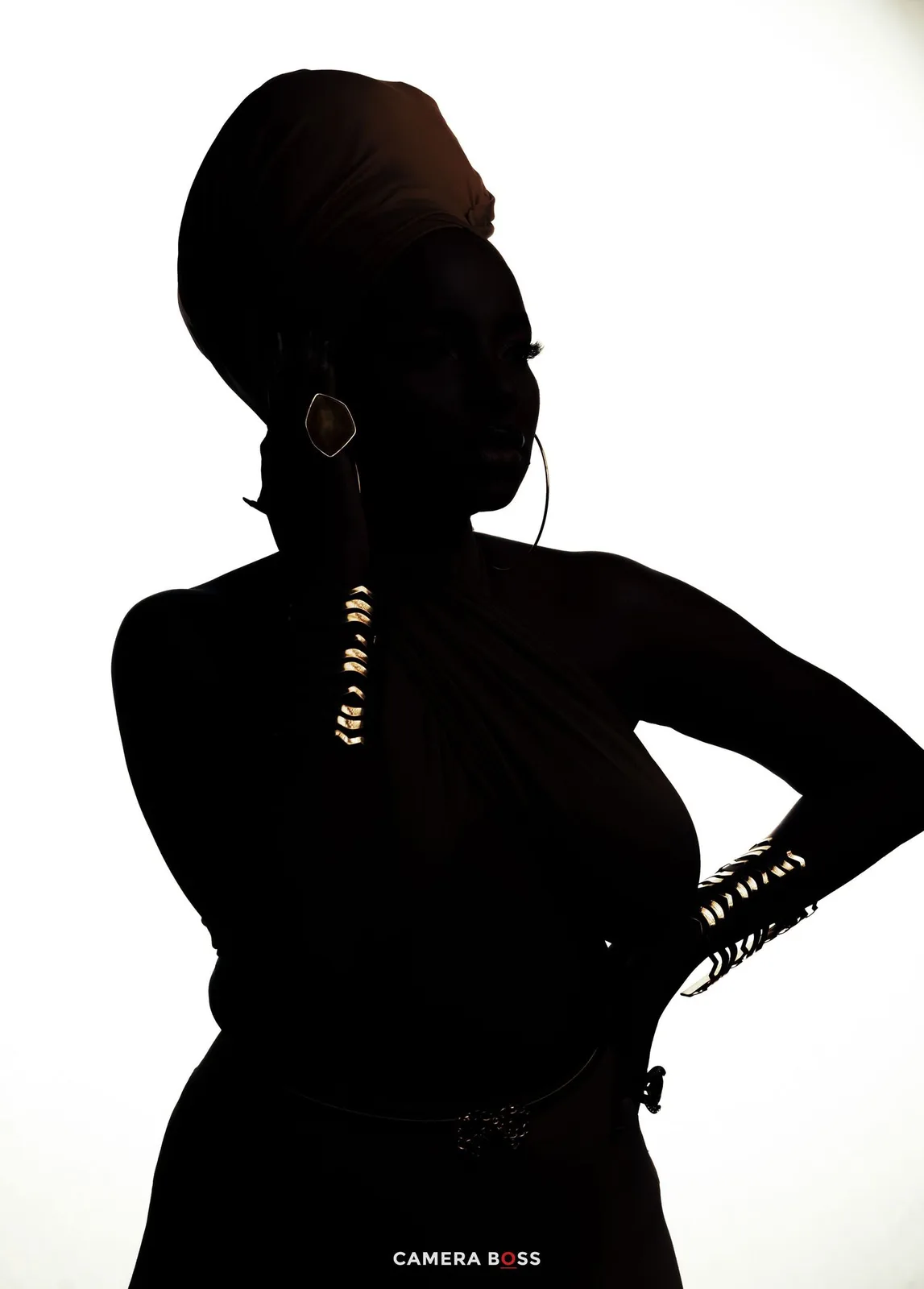 Dramatic silhouette of a person wearing beaded accessories against a white background, standing with hand on hip.
