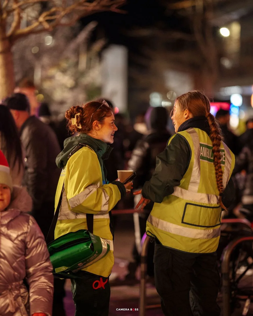 Security personnel in high-visibility yellow vests patrol a crowded nighttime street event.