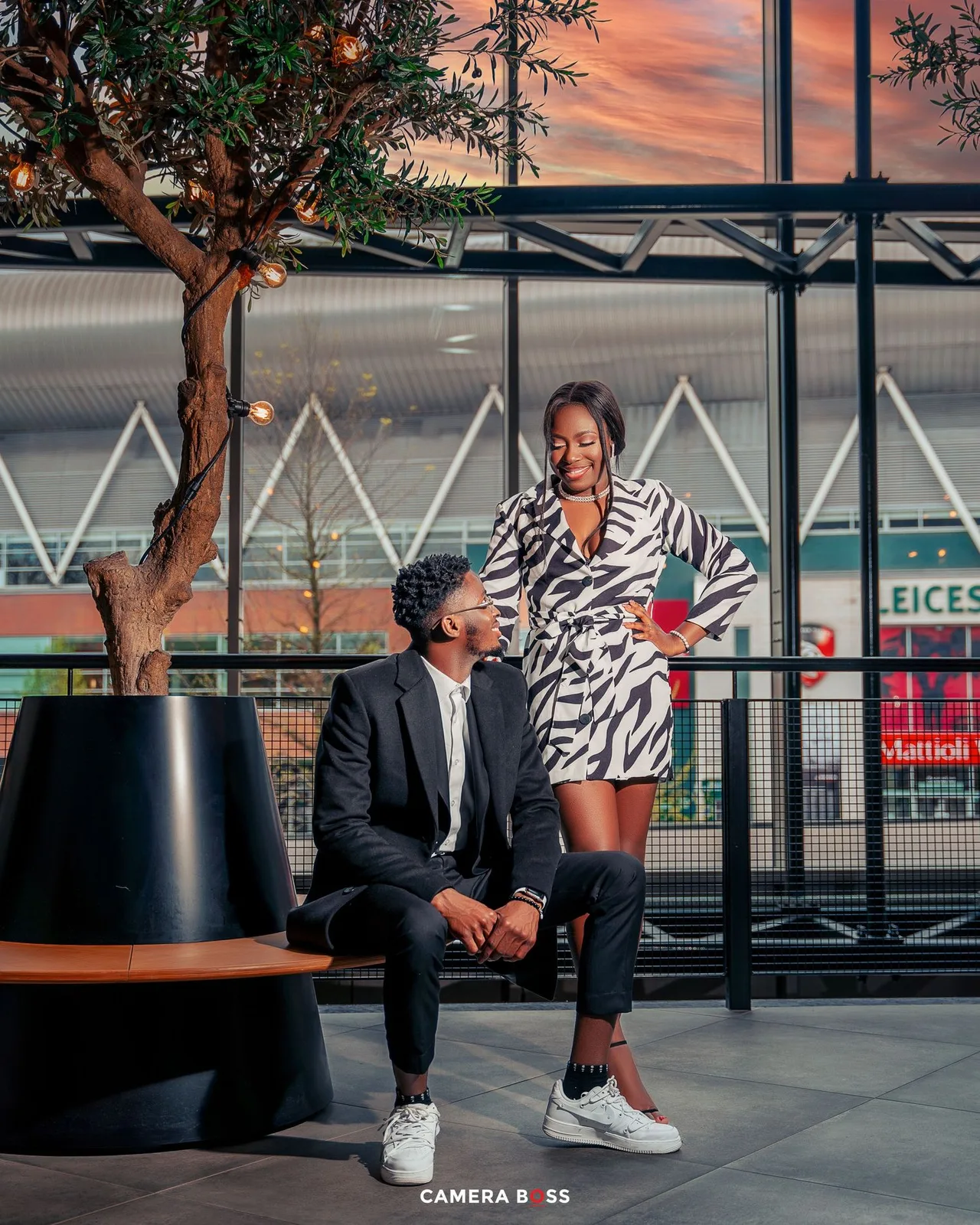 Stylish couple poses together at sunset against urban backdrop with modern architecture and tree.