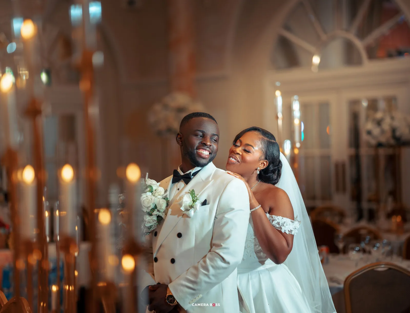 A happy couple shares a joyful moment together in a luxurious wedding venue with glowing candles and elegant decor.