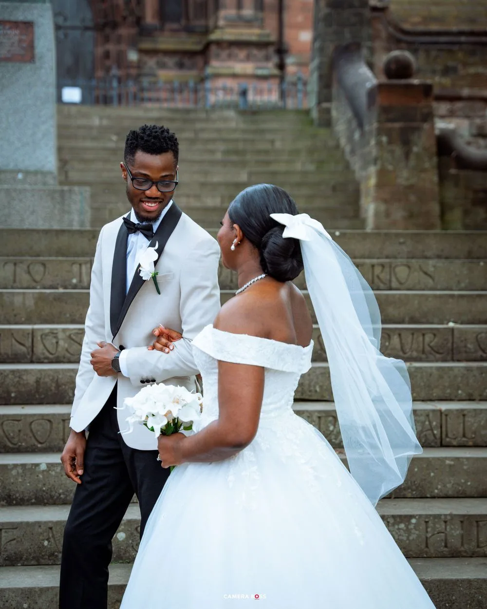 A wedding couple poses on stone steps outside a historic brick church with the bride in a flowing white gown.