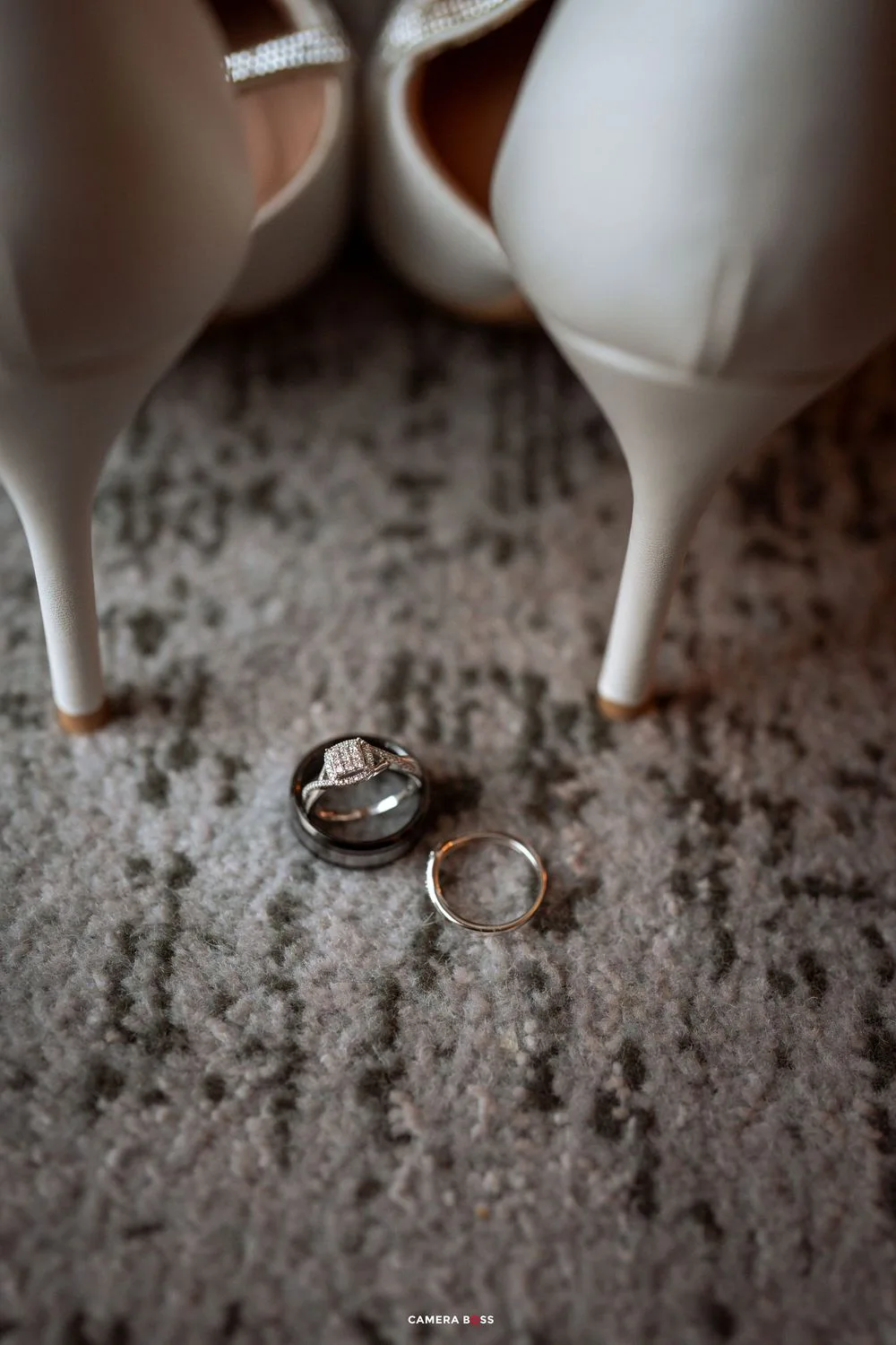 Wedding rings photographed on a textured stone surface with ceramic figurines in the background.