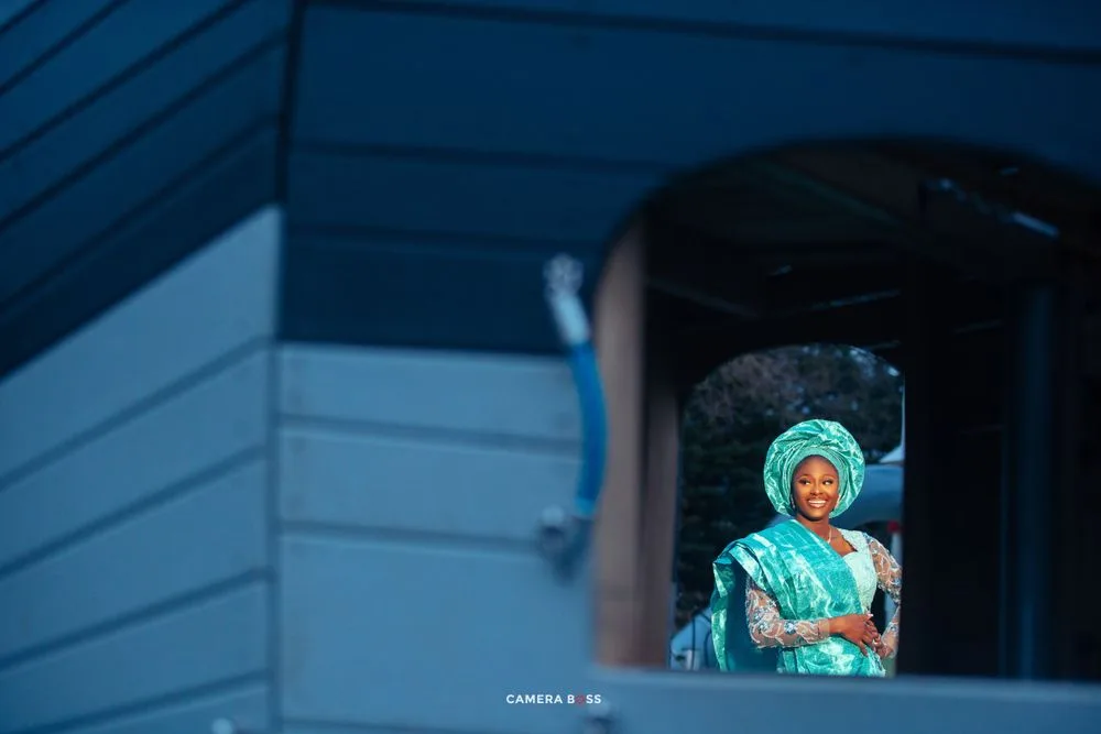 A person wearing turquoise medical scrubs and surgical cap looks through a window with blue framing.