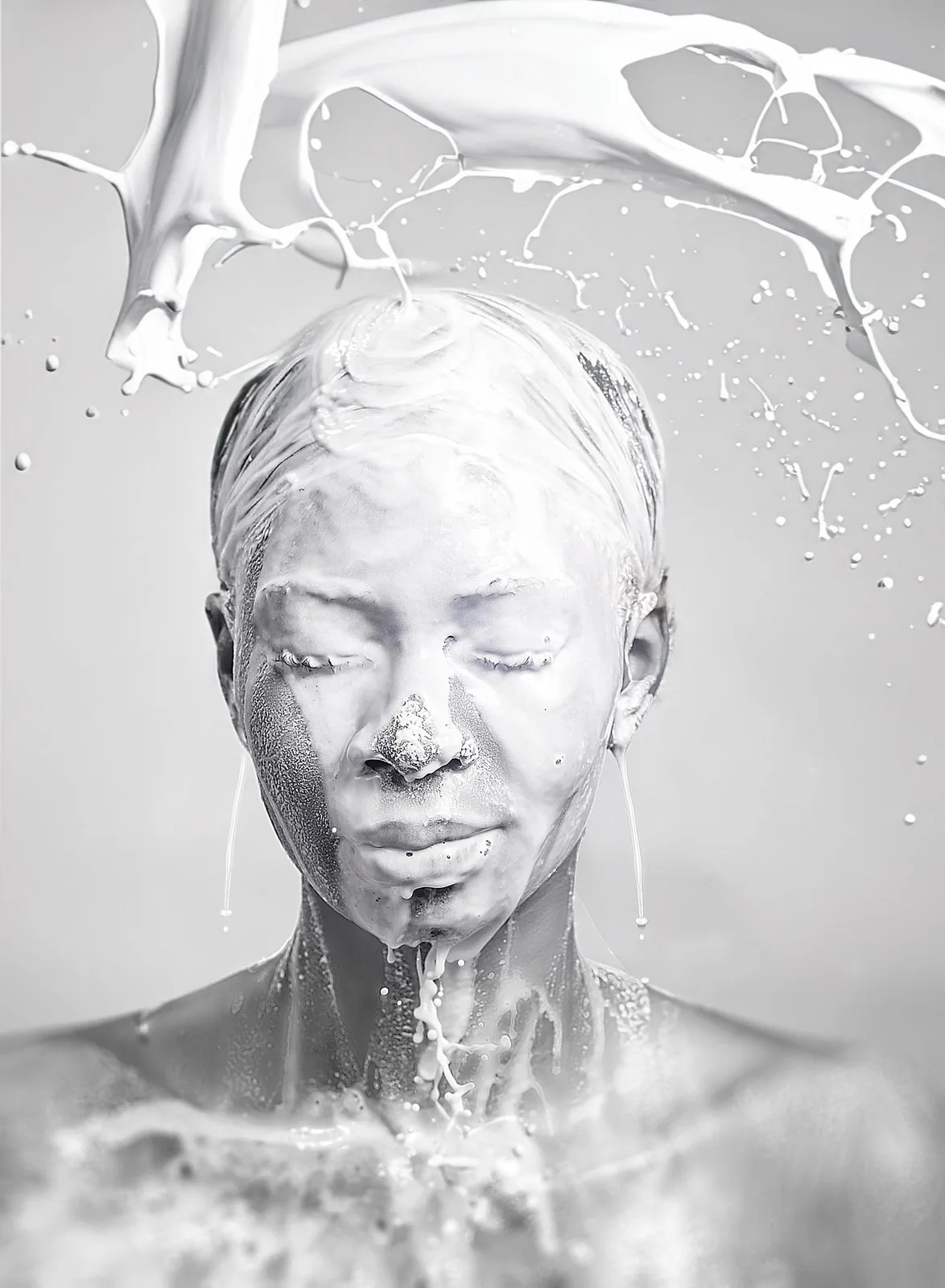 Artistic black and white portrait of figure covered in white paint with water splashing and dripping down.