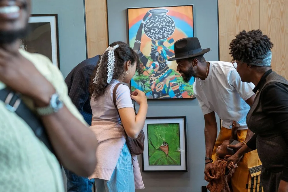 People viewing colorful artwork at an art gallery exhibition, engaging with paintings on display.