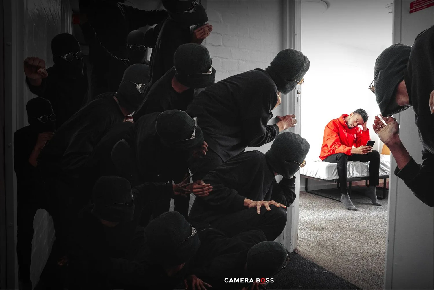 Silhouetted figures in dark clothing kneel in a stark room while a pop of red stands out in selective coloring.