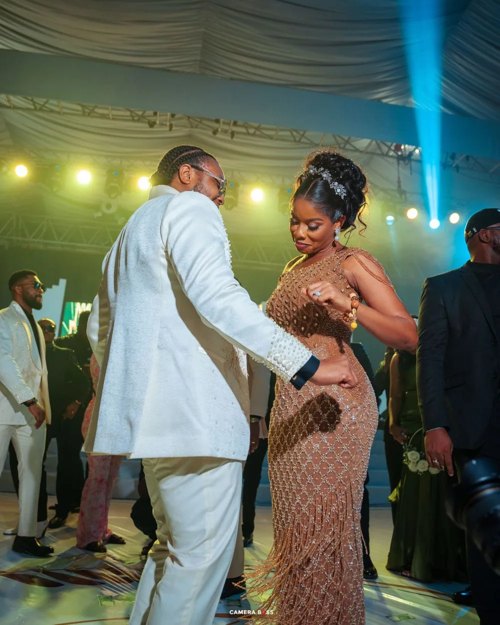 A couple dances together at an elegant event under a tent with mood lighting and a white-draped ceiling.