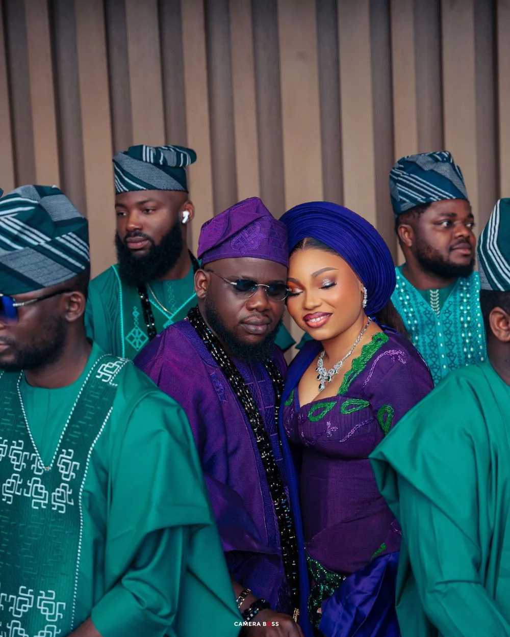 Group wearing traditional West African attire in purple and emerald green poses together for formal portrait.