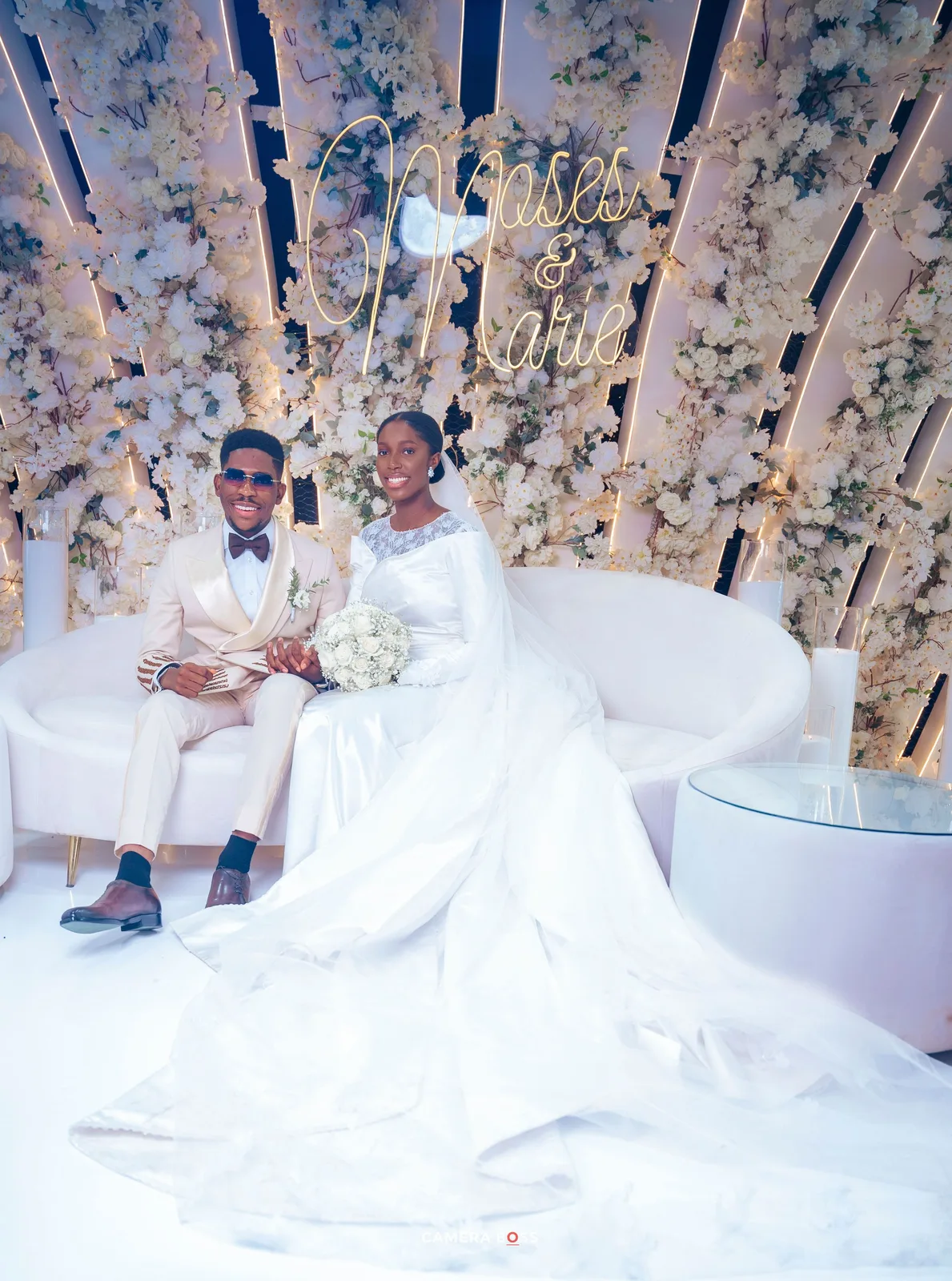 A stunning wedding scene with a long white gown against an elegant backdrop of floral arrangements and white draping.