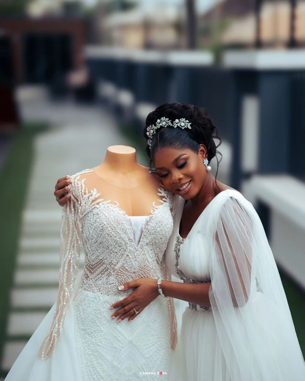 A bride admiring a white beaded wedding dress on a mannequin while wearing elegant wedding attire.