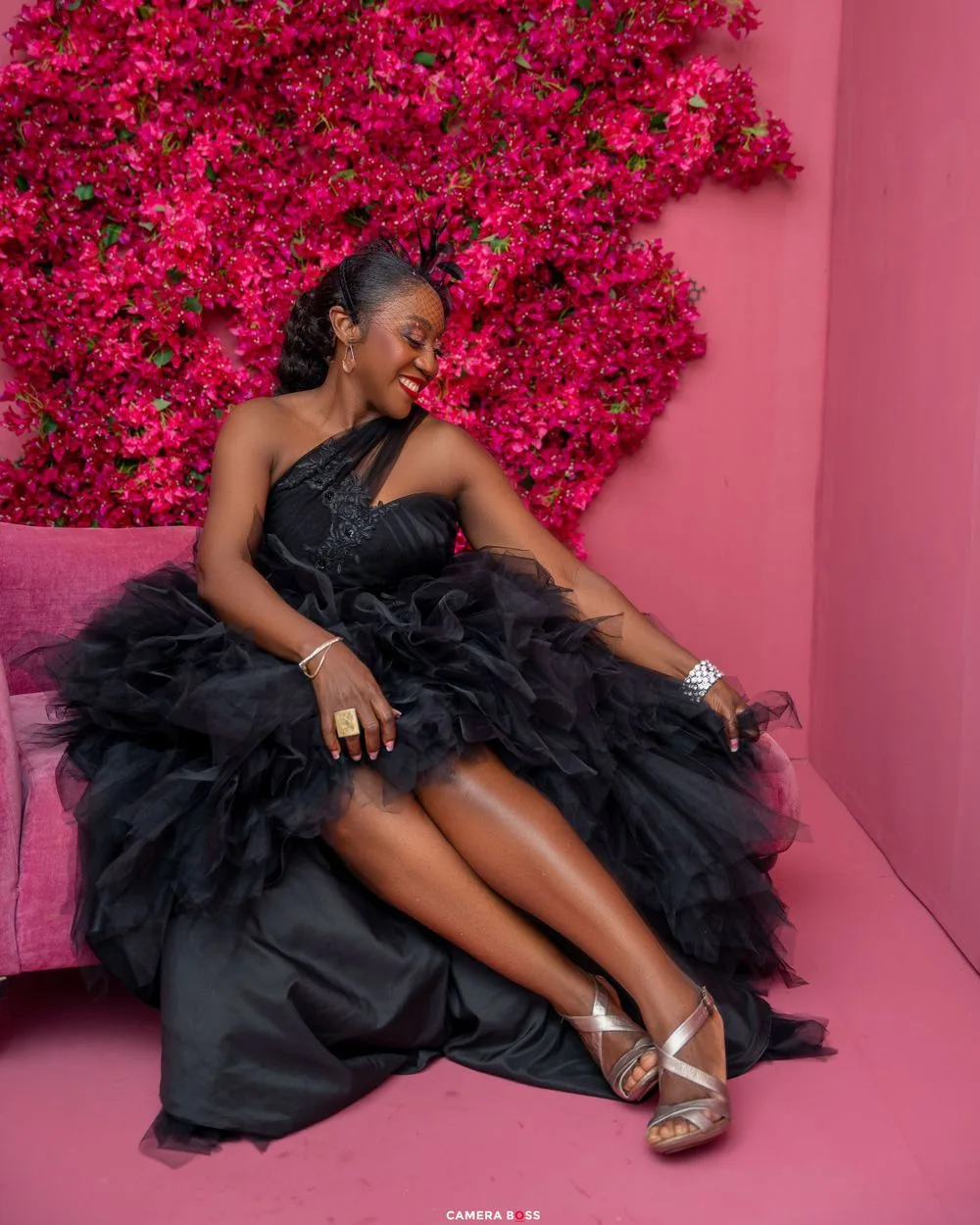 A glamorous black tulle gown is set against a pink wall with bright magenta flowers creating a stunning contrast.
