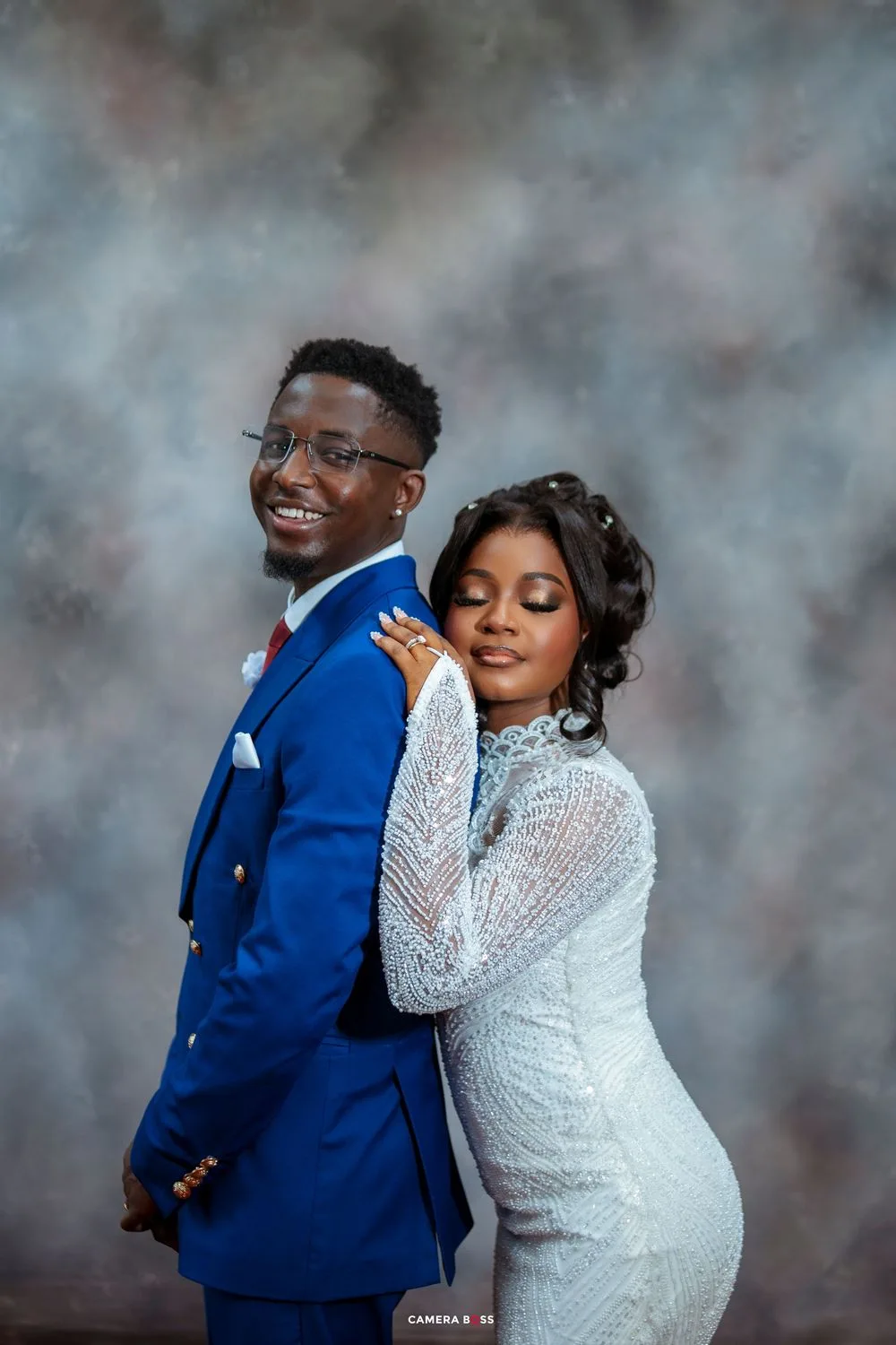 A couple in wedding attire, with the groom in royal blue suit and bride in white lace dress, pose for a romantic portrait.