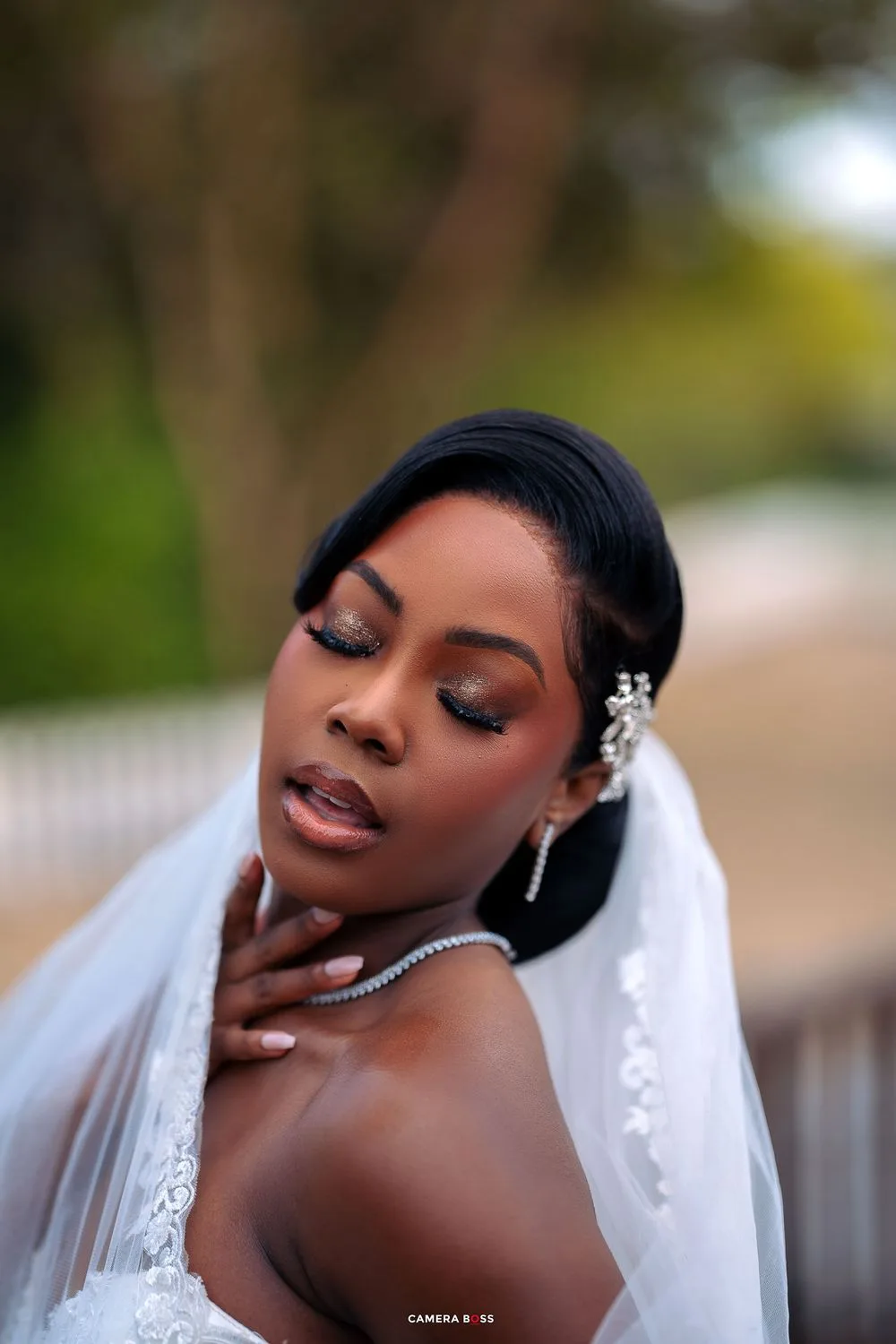A bride wearing elegant makeup, a veil and crystal earrings poses with eyes closed in an artistic bridal portrait.