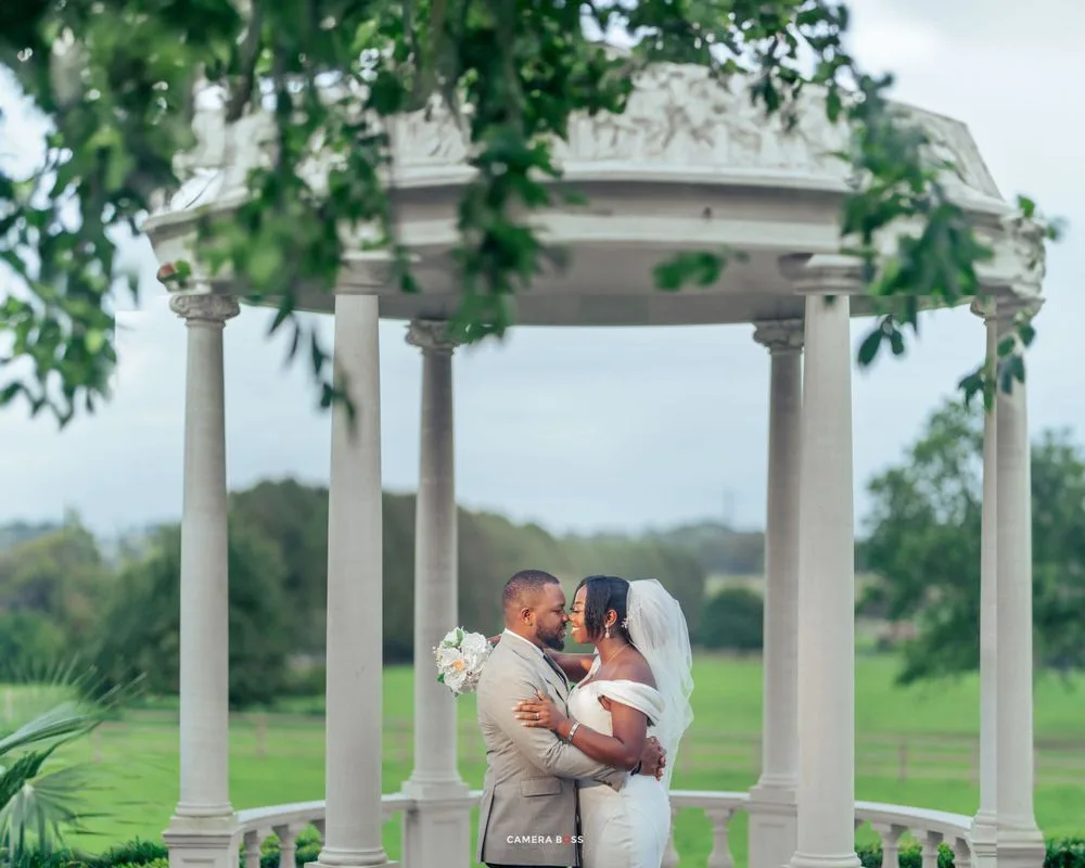 A couple shares a romantic kiss under an elegant white gazebo overlooking a lush green golf course.