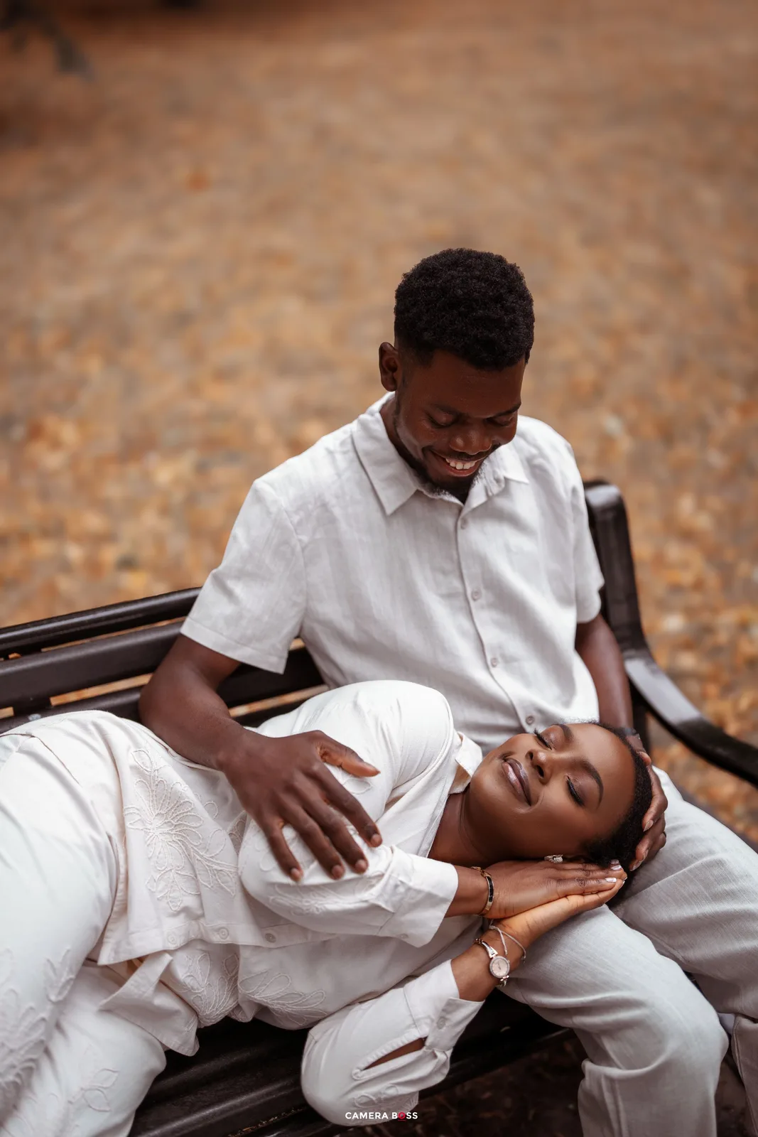 A couple in white outfits shares intimate moments while lying together on a rustic wooden surface outdoors.