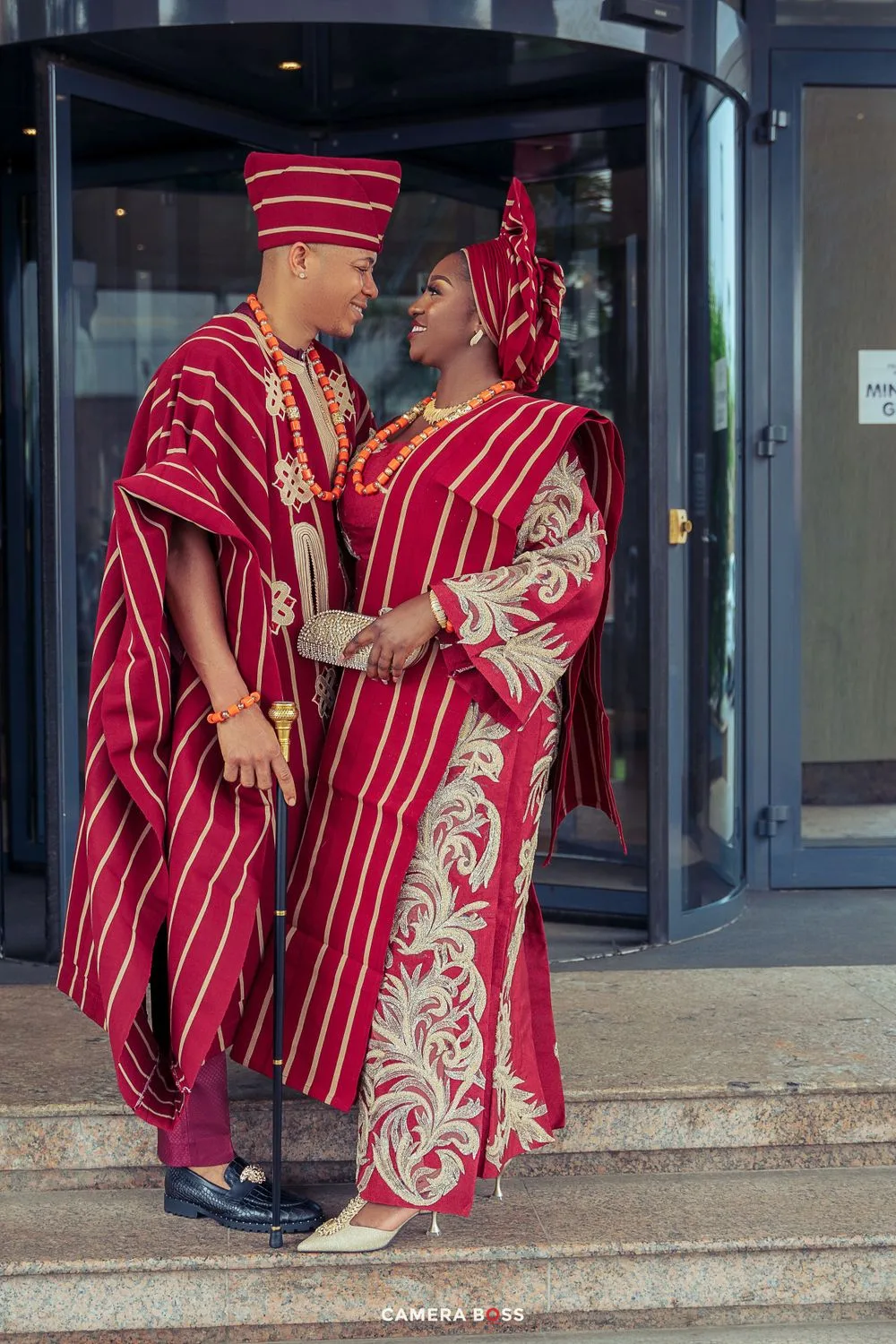 Couple wearing matching red and white traditional African attire sitting on stone steps.