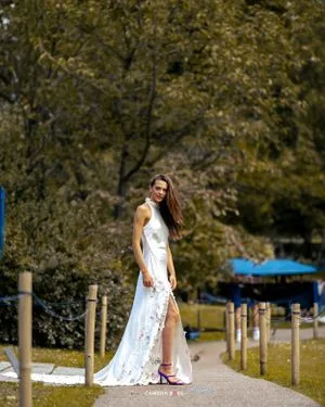 A person in a flowing white lace dress walks on a garden path surrounded by autumn foliage.