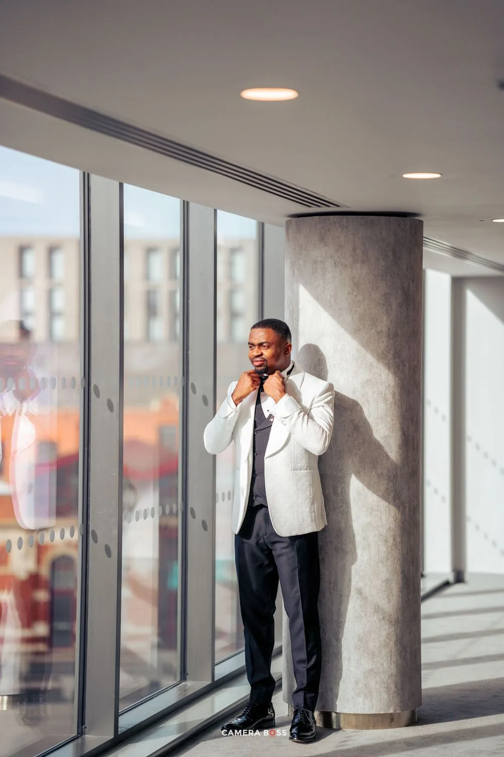 Professional in a white blazer stands near large windows in modern office building with city view and natural lighting.