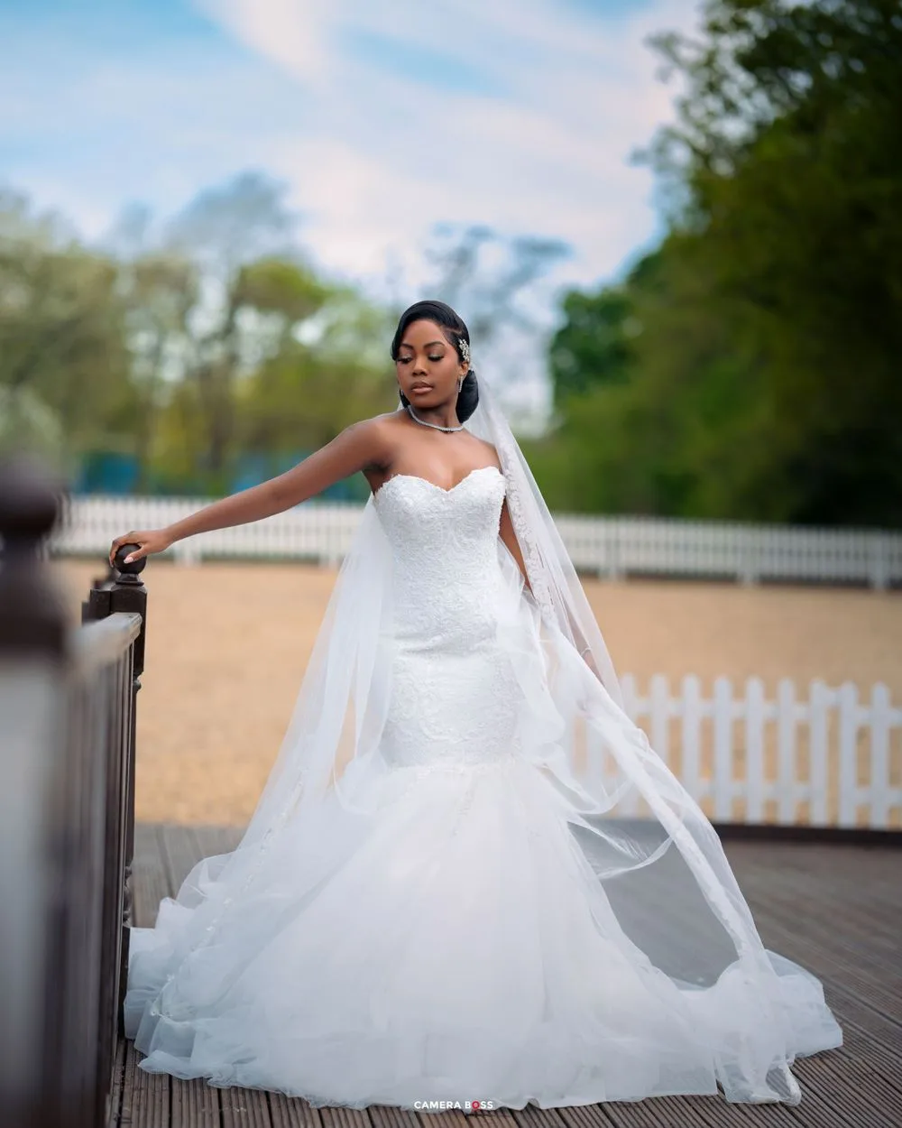 Beautiful wedding dress with sweetheart neckline, flowing train and veil captured on a wooden deck with picket fence backdrop.