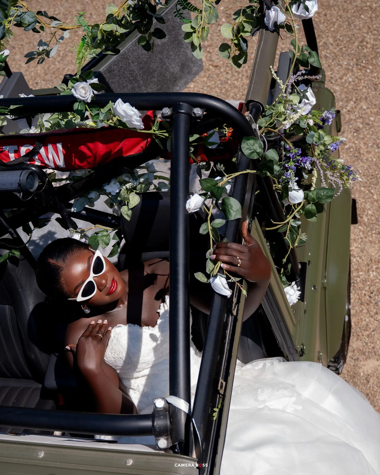 A couple snuggling and laughing together in front of a greenery wall decorated with white flowers.