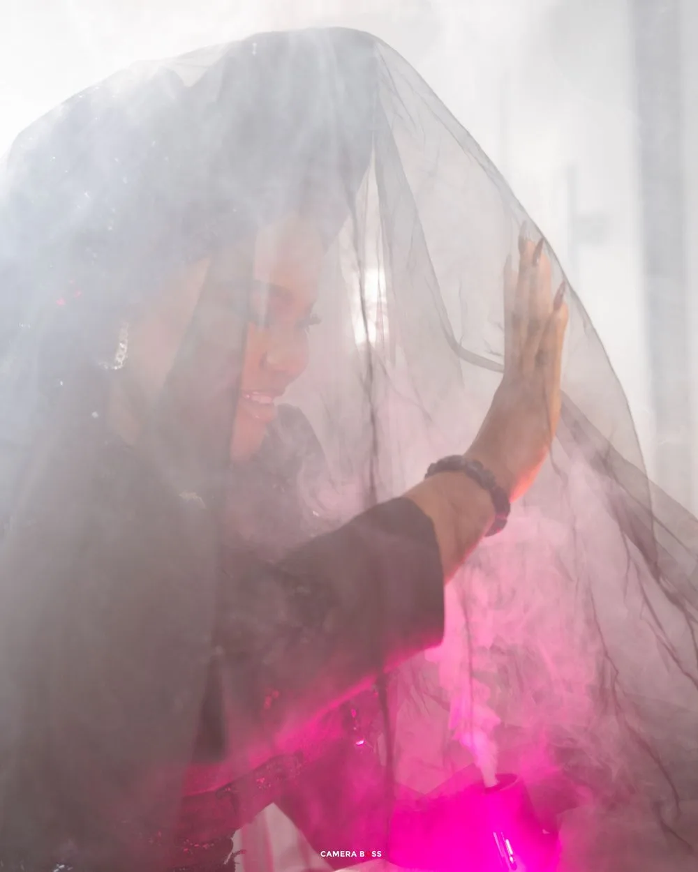 Figure covered by sheer fabric with pink light glowing from beneath creates an ethereal artistic composition.