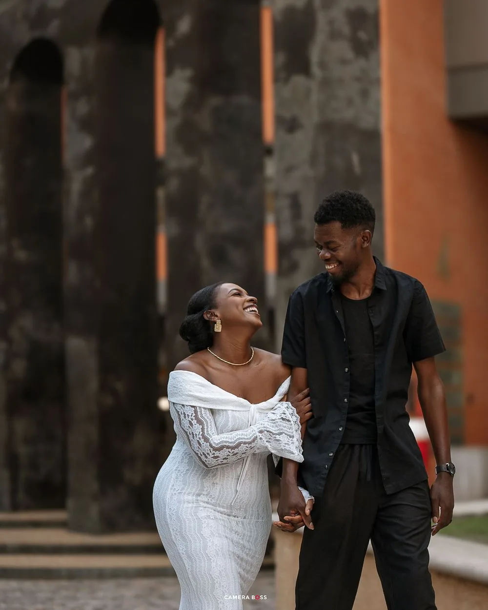 A couple in formal attire shares a joyful moment together while walking outdoors.