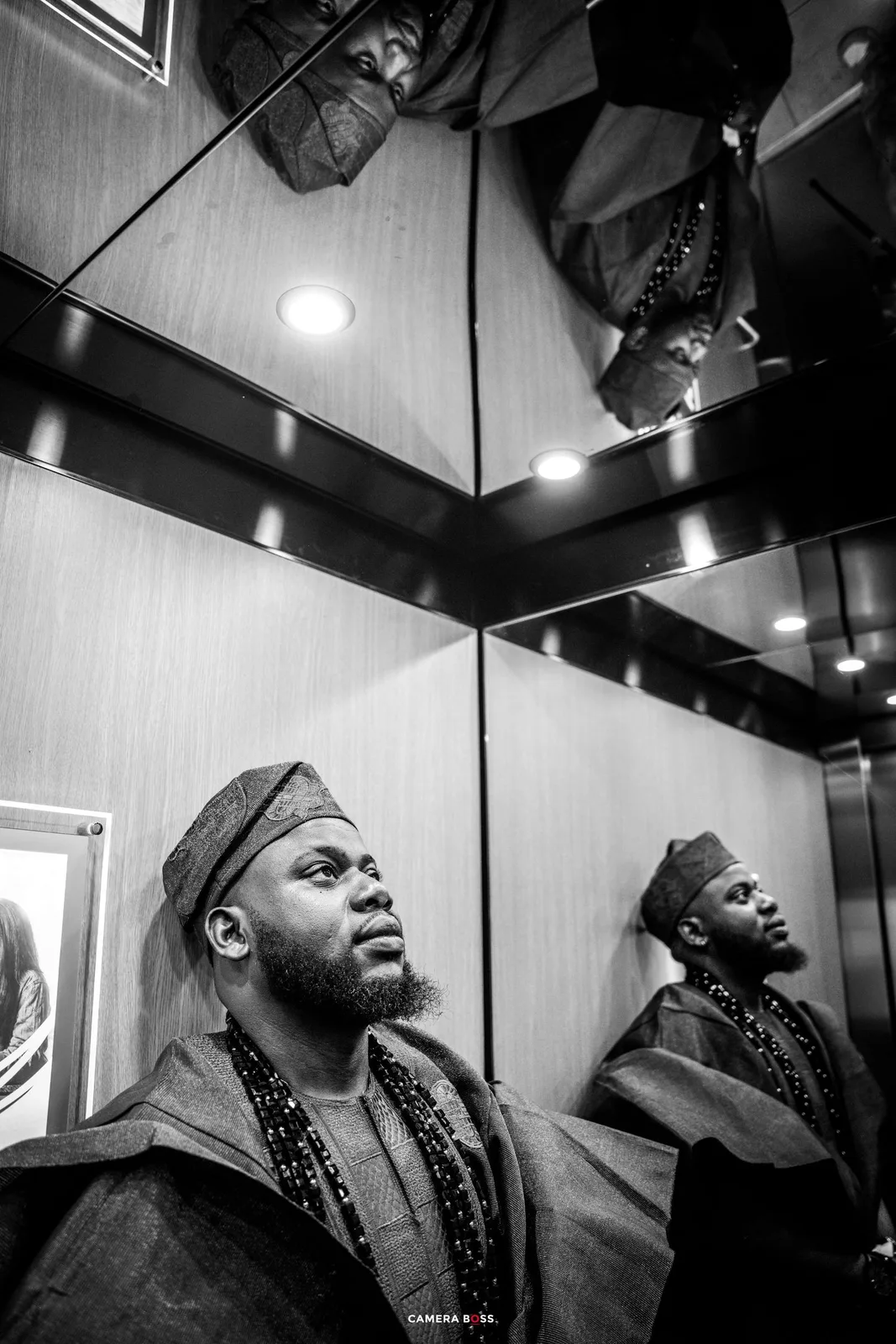 Black and white photo showing reflections in an elevator mirror with overhead lighting and geometric interior details.