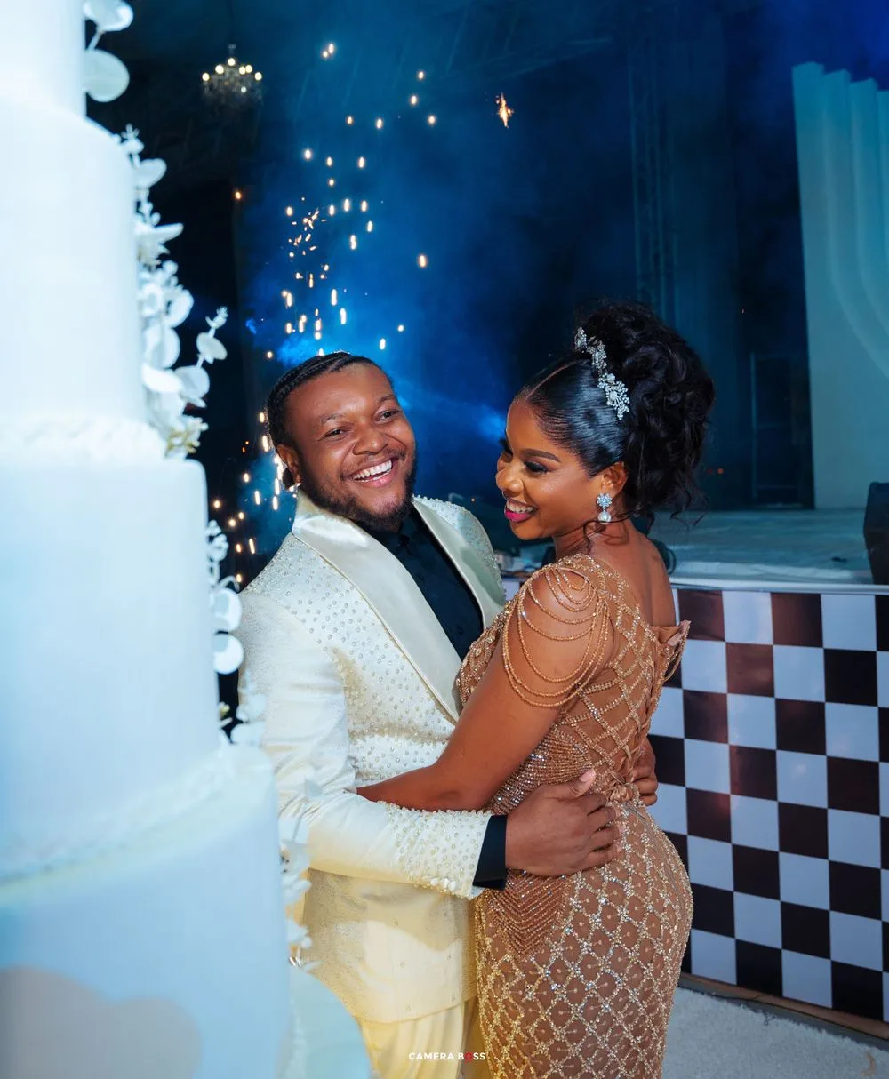 A happy couple dances during their wedding reception, wearing elegant formal attire against a backdrop of twinkling lights.