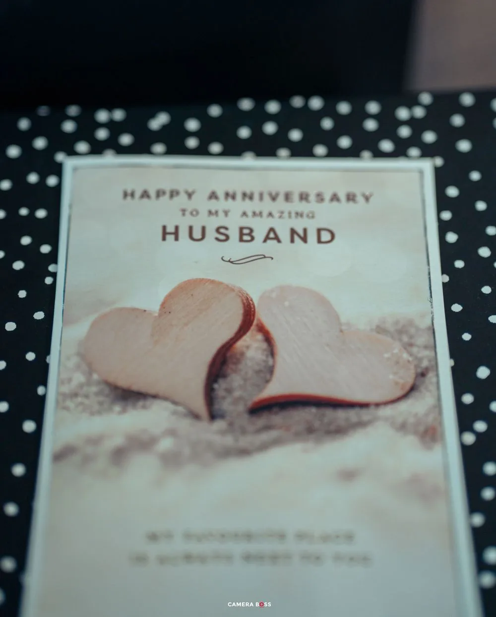Anniversary card reading 'Happy Anniversary to my amazing husband' with two pink paper hearts on polka dot background.