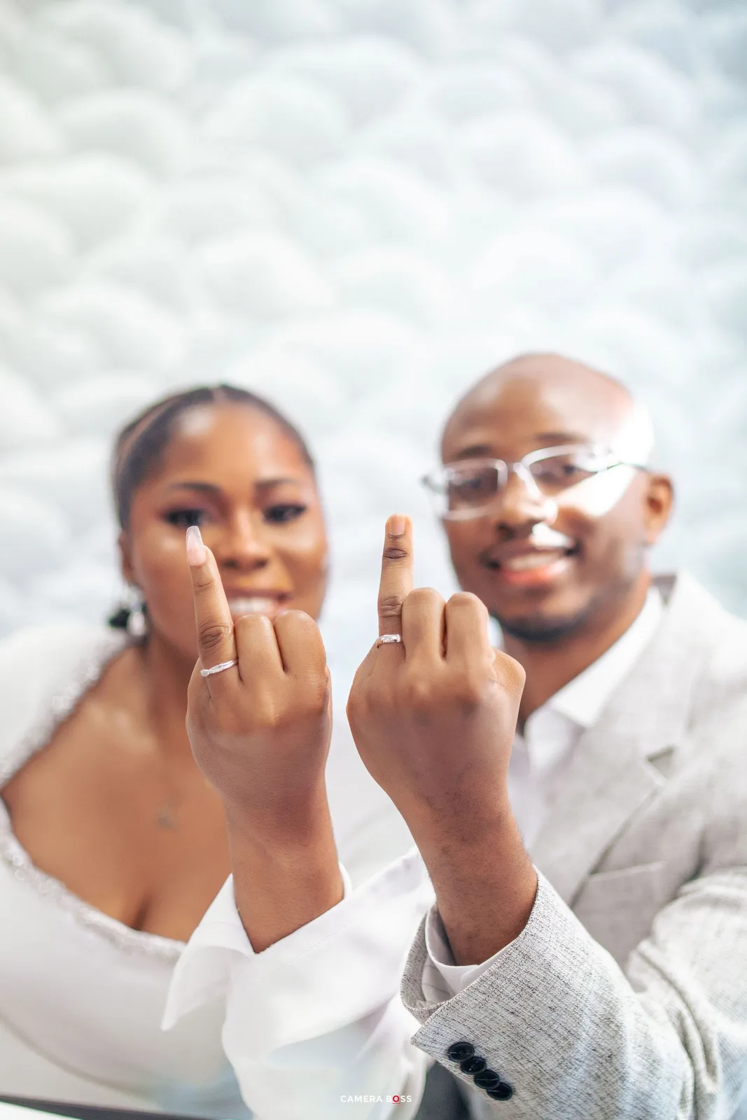 A happy couple showing off their wedding rings to the camera while smiling.