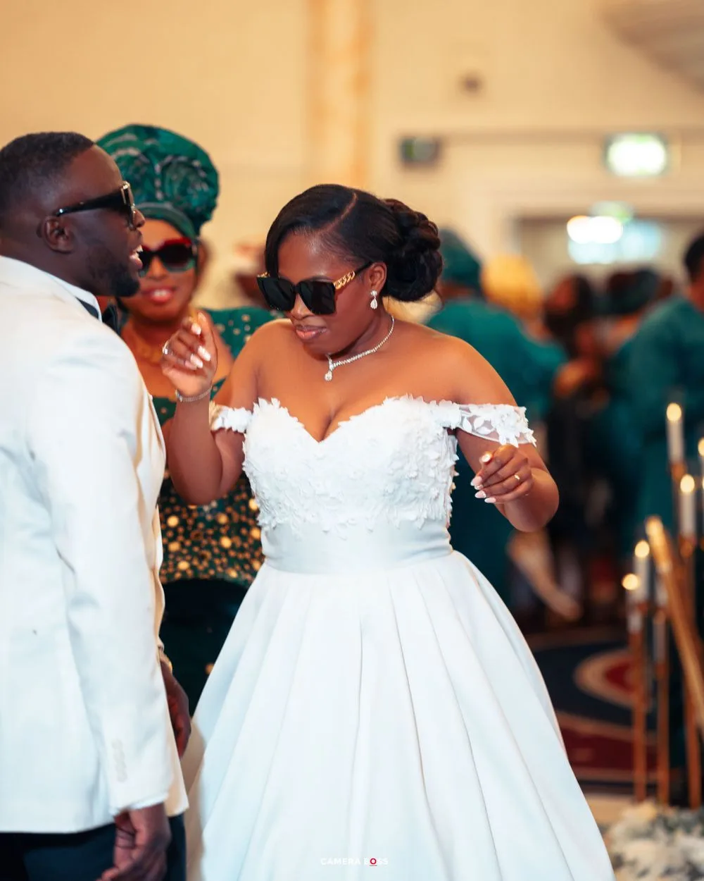 A bride in a stunning white off-shoulder wedding gown and sunglasses dancing at her wedding celebration.