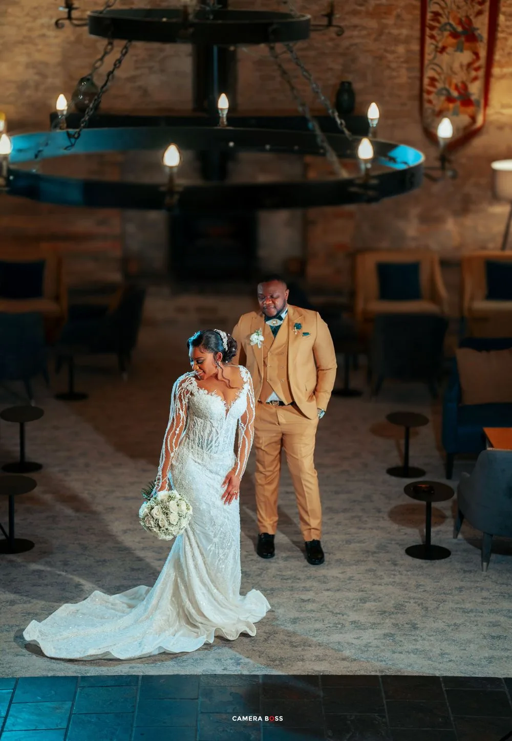 Wedding couple in a rustic venue with stone walls and wrought iron chandelier, lit by glowing candles.