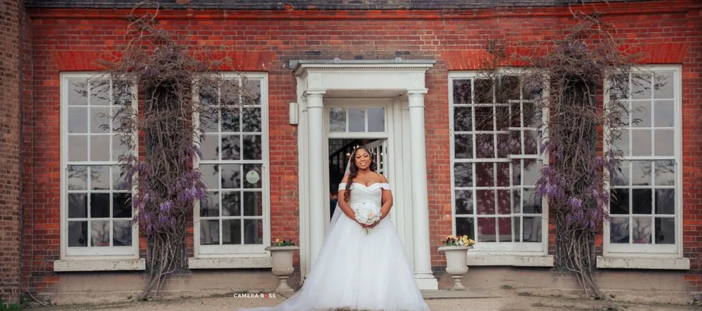 Elegant bridal portrait framed in white doorway with purple wisteria vines and symmetrical windows on brick facade.