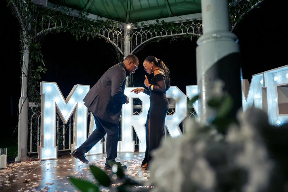 A couple dances under an ornate gazebo with illuminated 'MR' letters glowing in the background.