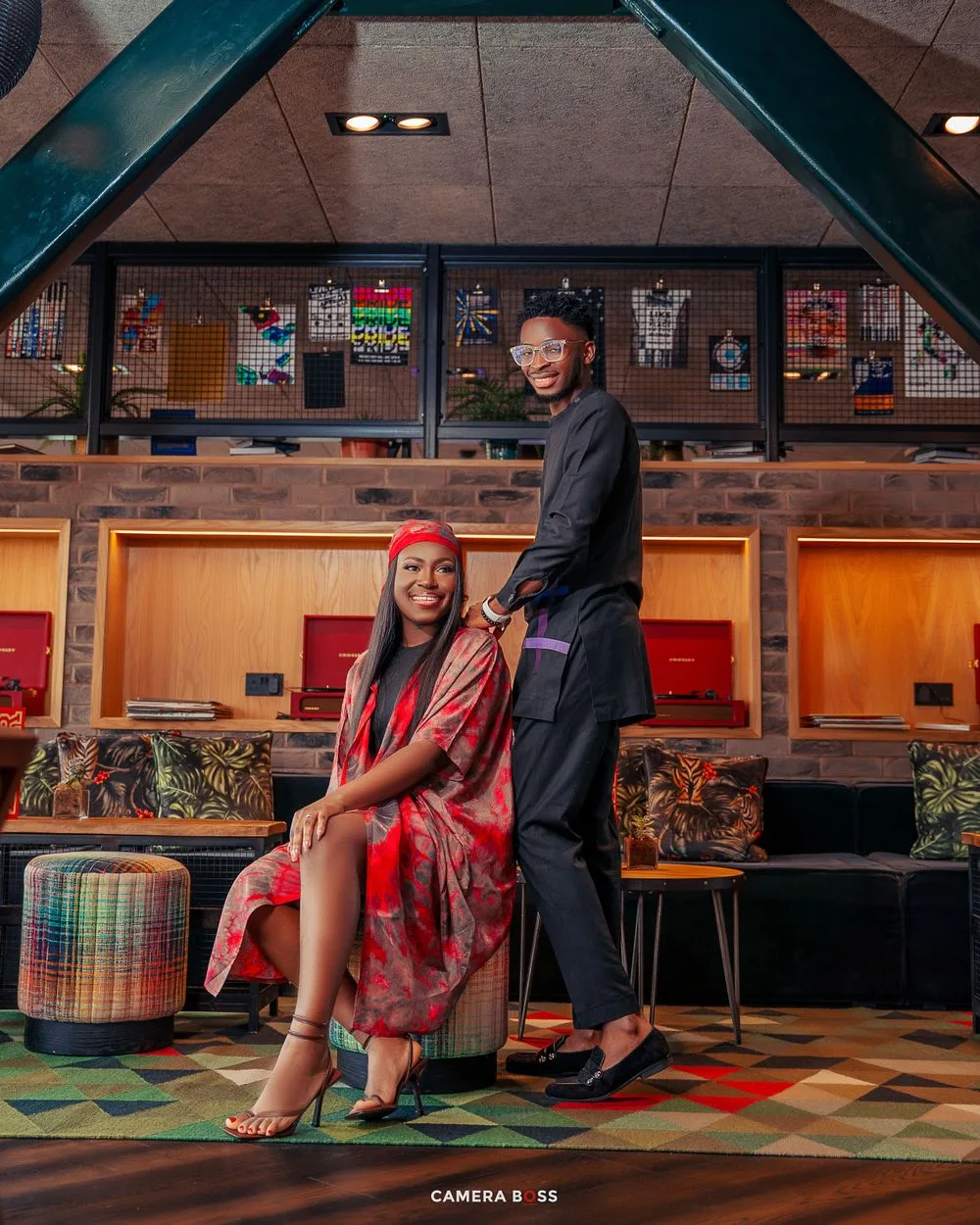 A couple poses together in a stylish restaurant interior with colorful geometric flooring and wooden bar seating.