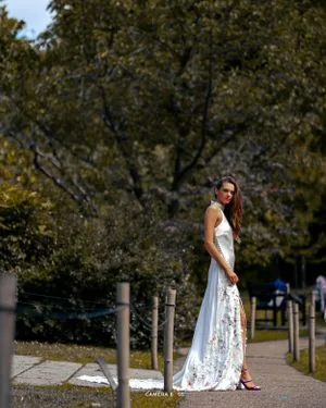 Someone in an elegant white lace maxi dress stands on a pathway under autumn trees in a park setting.