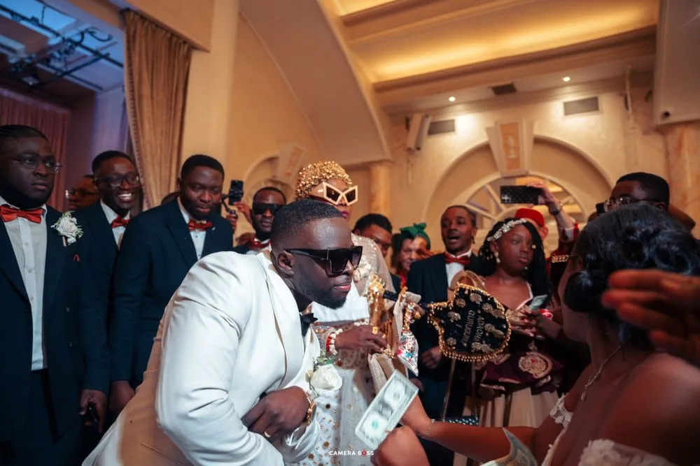 Energetic wedding reception moment with performer in white suit entertaining guests while surrounded by crowd.
