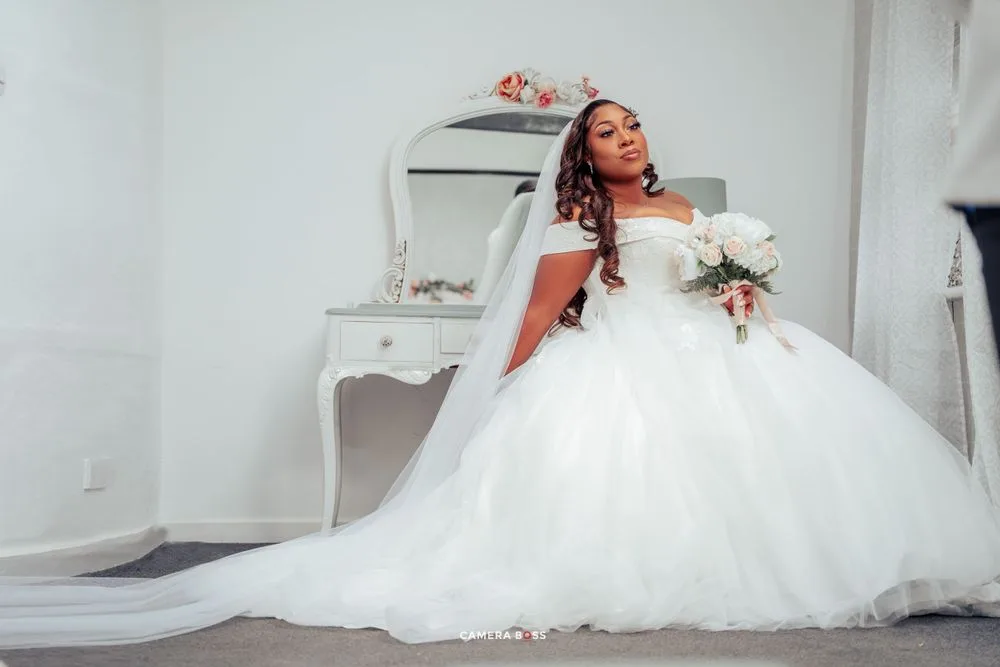 A stunning bride in a voluminous white ball gown relaxes on the floor beside an elegant vanity table.