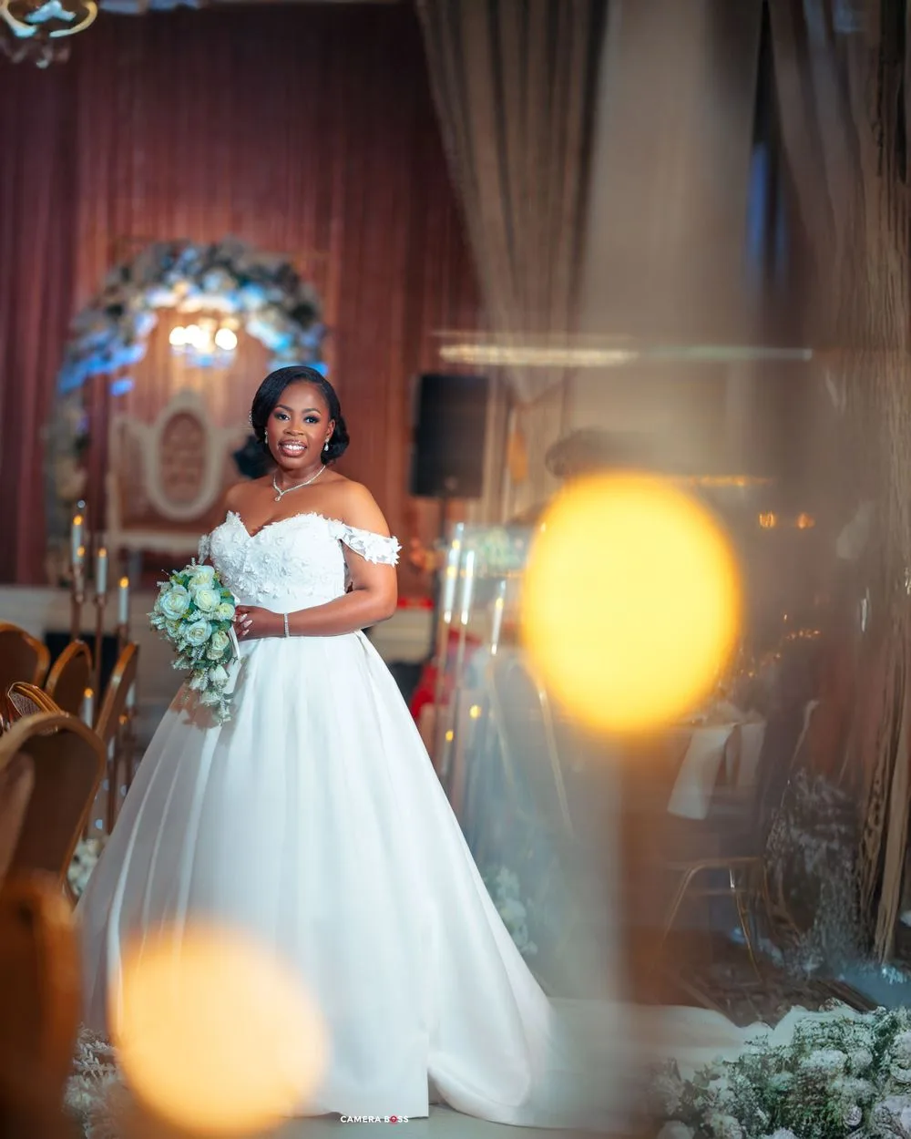 A bride in a stunning off-shoulder white ballgown stands at the altar, holding a mint green and white bouquet.