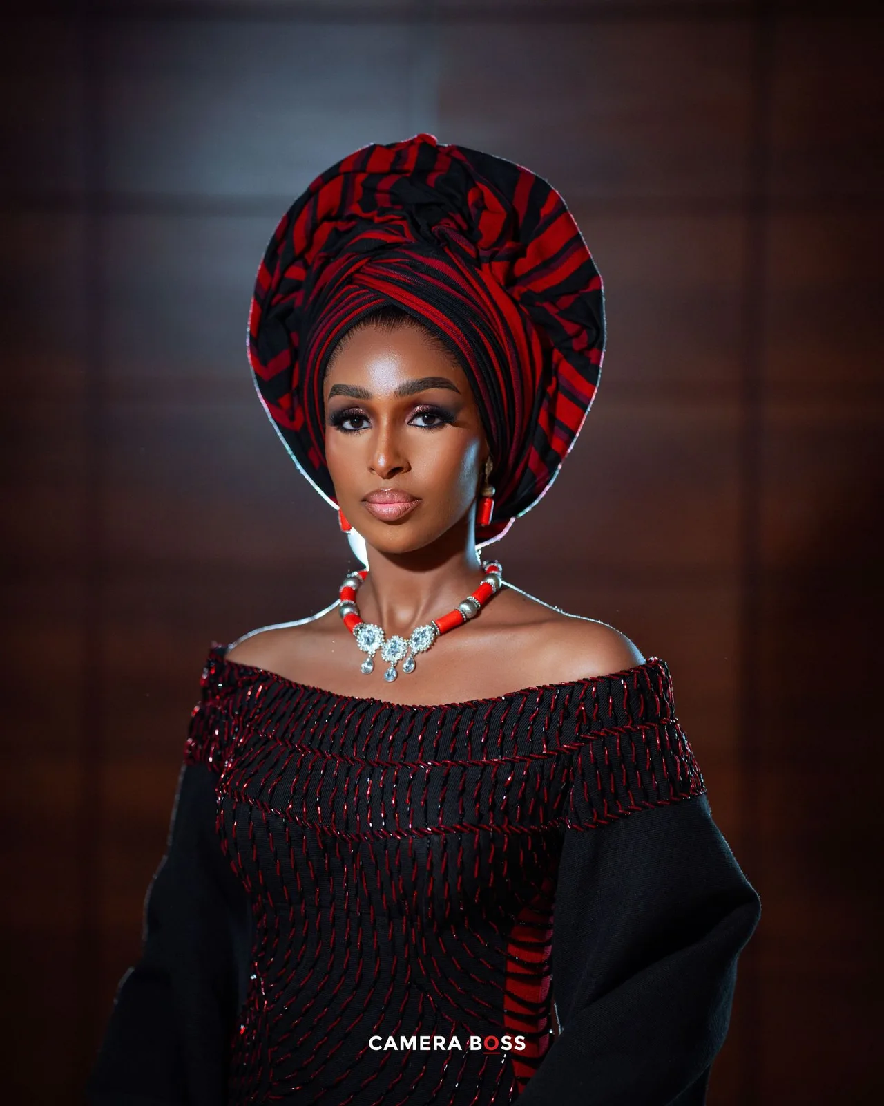 Elegant portrait of a person in a black and red off-shoulder dress with matching headwrap and statement necklace.