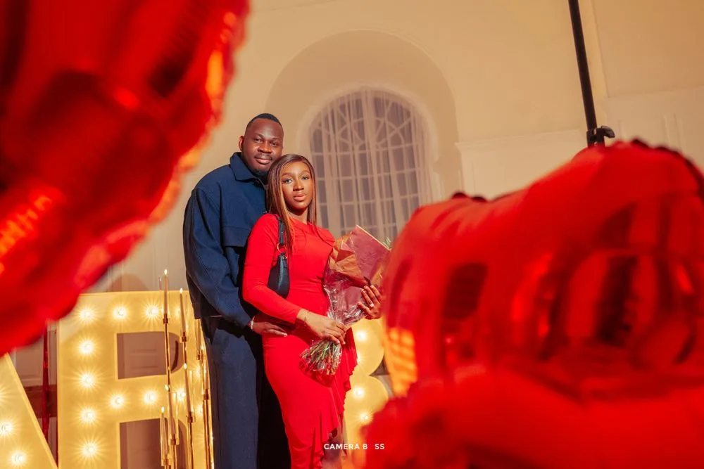 A couple wearing matching red outfits poses together with glowing lights in the background.