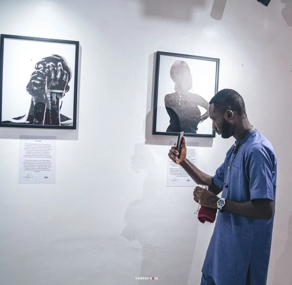 A person wearing blue views photographs displayed in a gallery with framed black and white portraits on the wall.