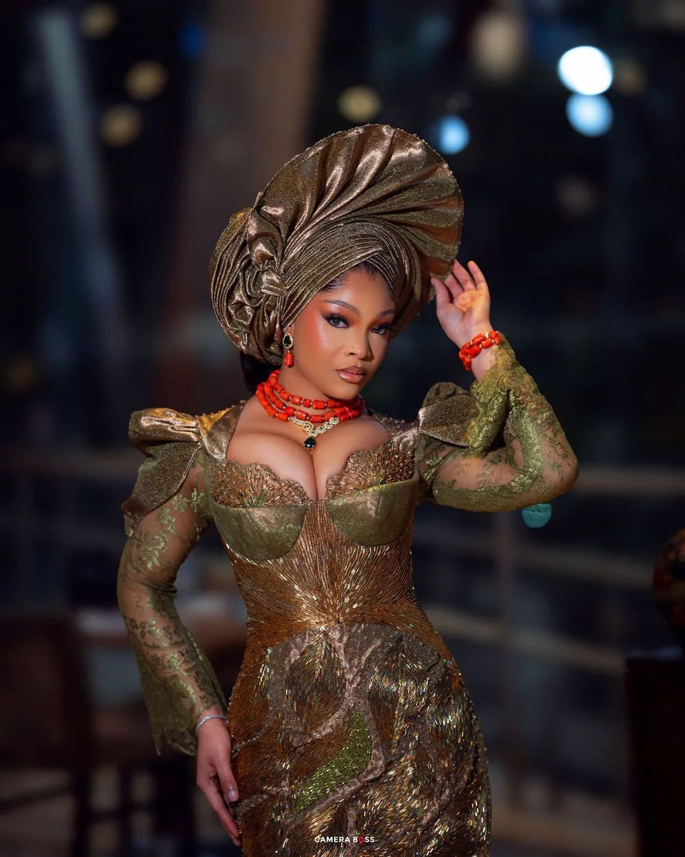 Glamorous portrait in a metallic bronze dress with matching head wrap and red accents against dark background.