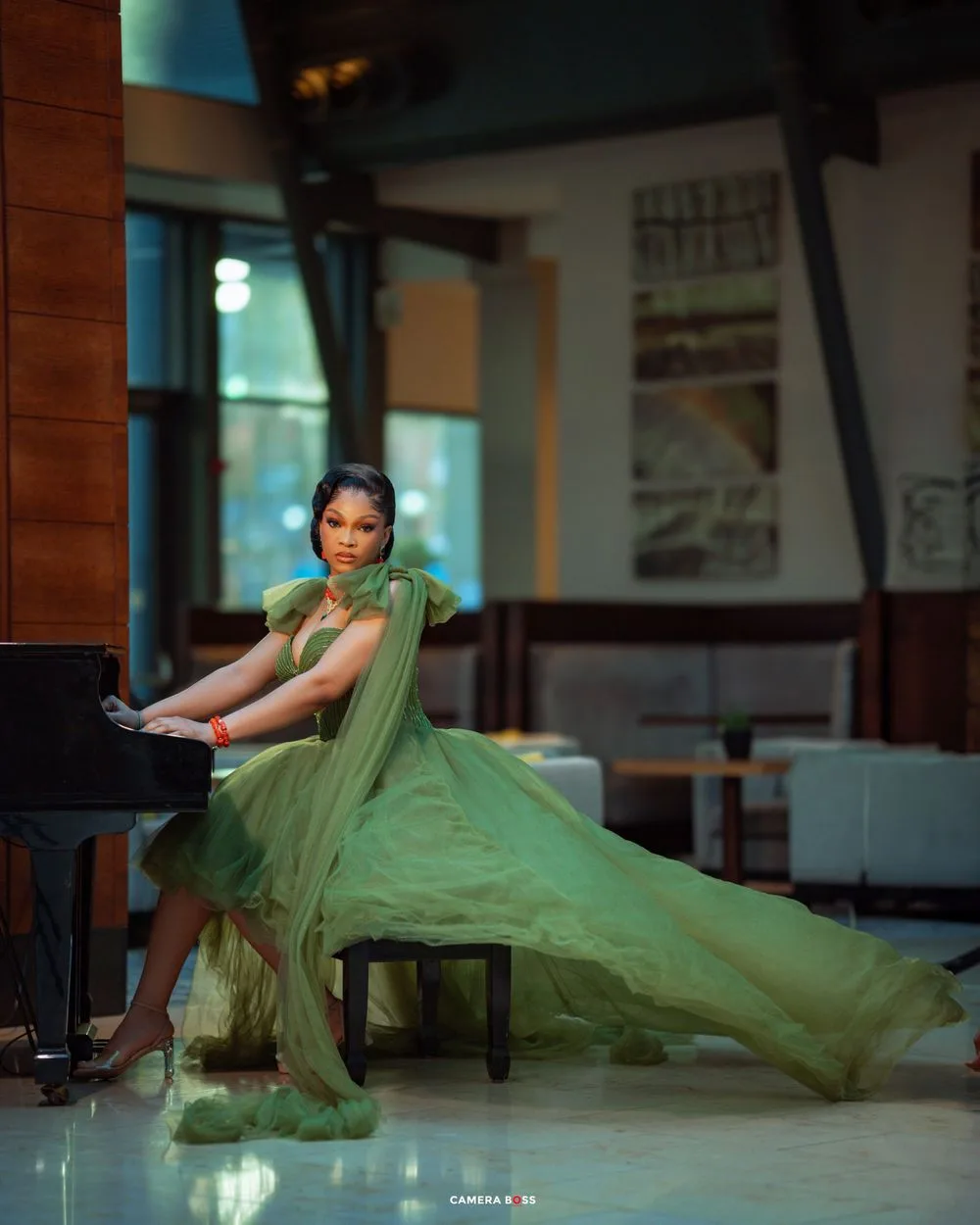 Dancer in flowing green gown performs elegantly next to grand piano in an interior space.