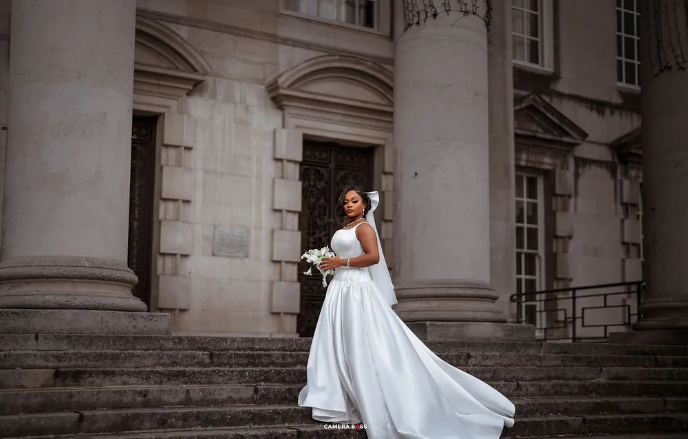 Bride in flowing white dress twirls gracefully on stone steps of historic building during wedding photoshoot.
