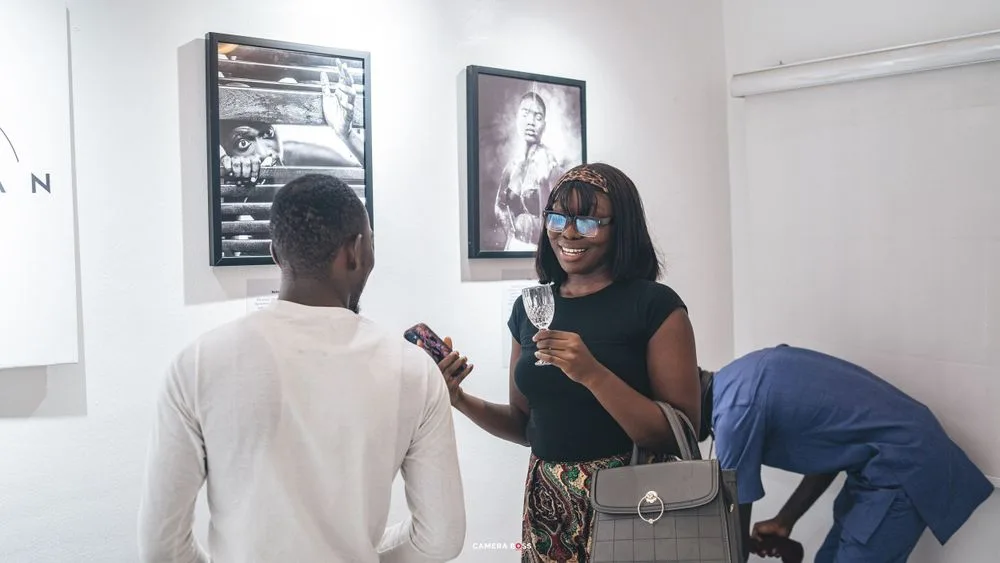 Three people conversing in an art gallery space with framed black and white photographs on the wall.