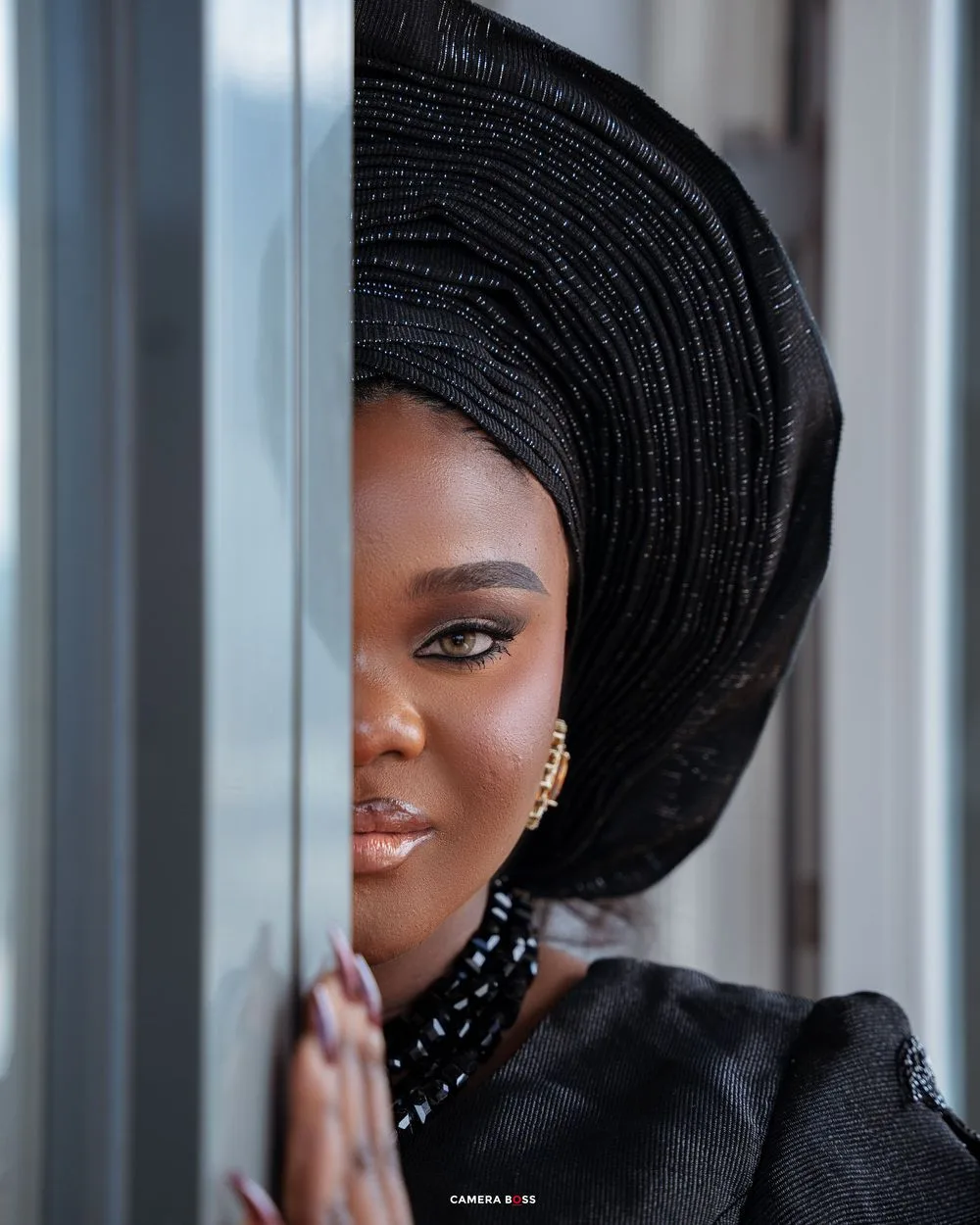 Elegant portrait in traditional black attire and dramatic headwrap against light background.