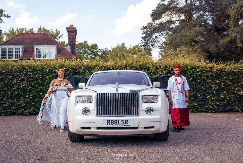 White Rolls Royce Phantom parked in front of a hedge with people standing beside it on a sunny day.